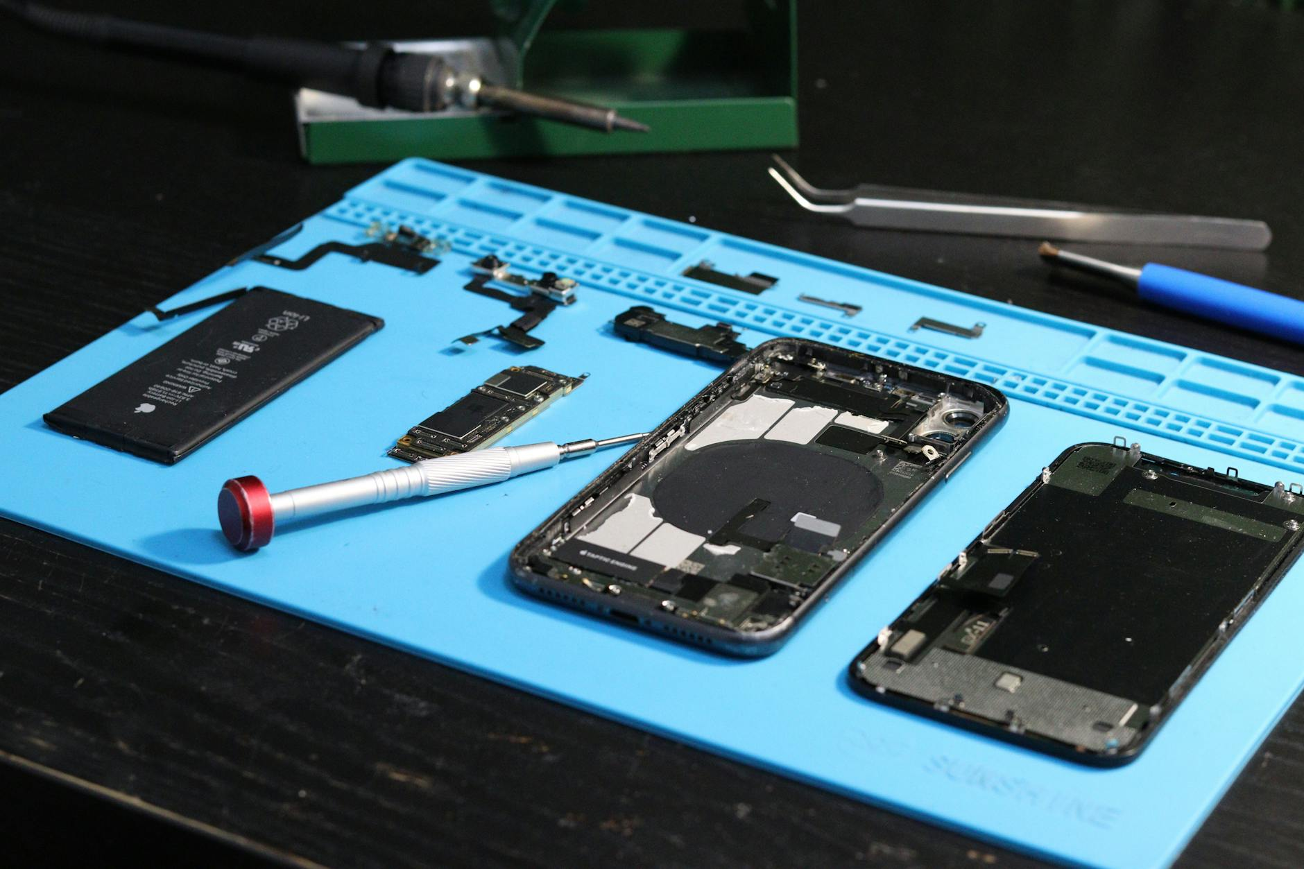Technician inspecting a smartphone at a workshop bench, illustrating used-device grading and functional testing.